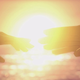 Two hands reach for each other against the backdrop of a sun's intensely bright light.